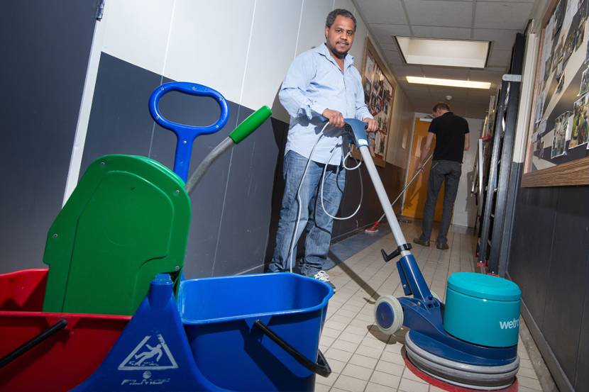 Schoonmaker in de gang bezig met de vloer boenen